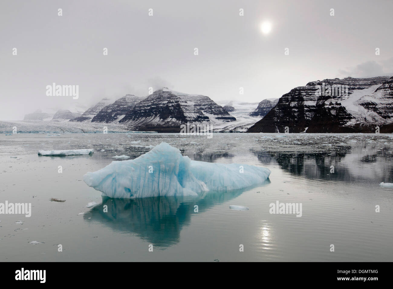 La riflessione di iceberg, scenario di montagna e il sole in un giorno nuvoloso, Vikingebugt, Scoresbysund, Sermersooq, Groenlandia Foto Stock