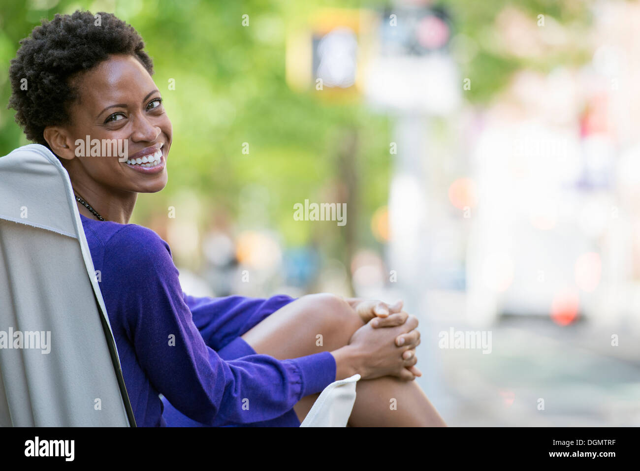 Città. Una donna in un vestito viola, seduta in una tela camping sedia, guardando sopra la sua spalla. Foto Stock