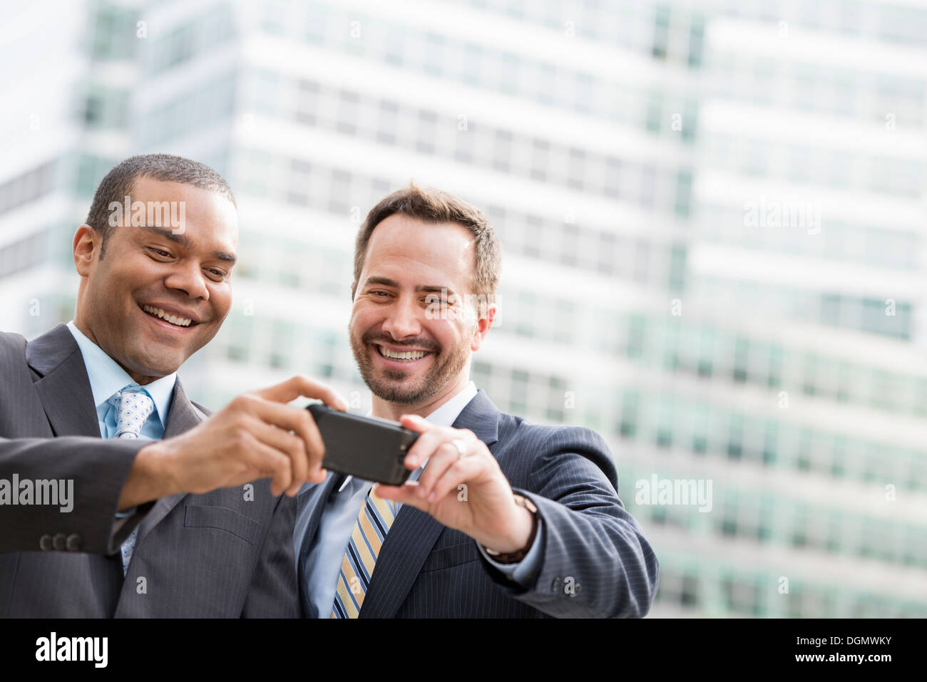 Città. Due uomini in abiti aziendali, guardando uno smart phone, sorridente. Foto Stock