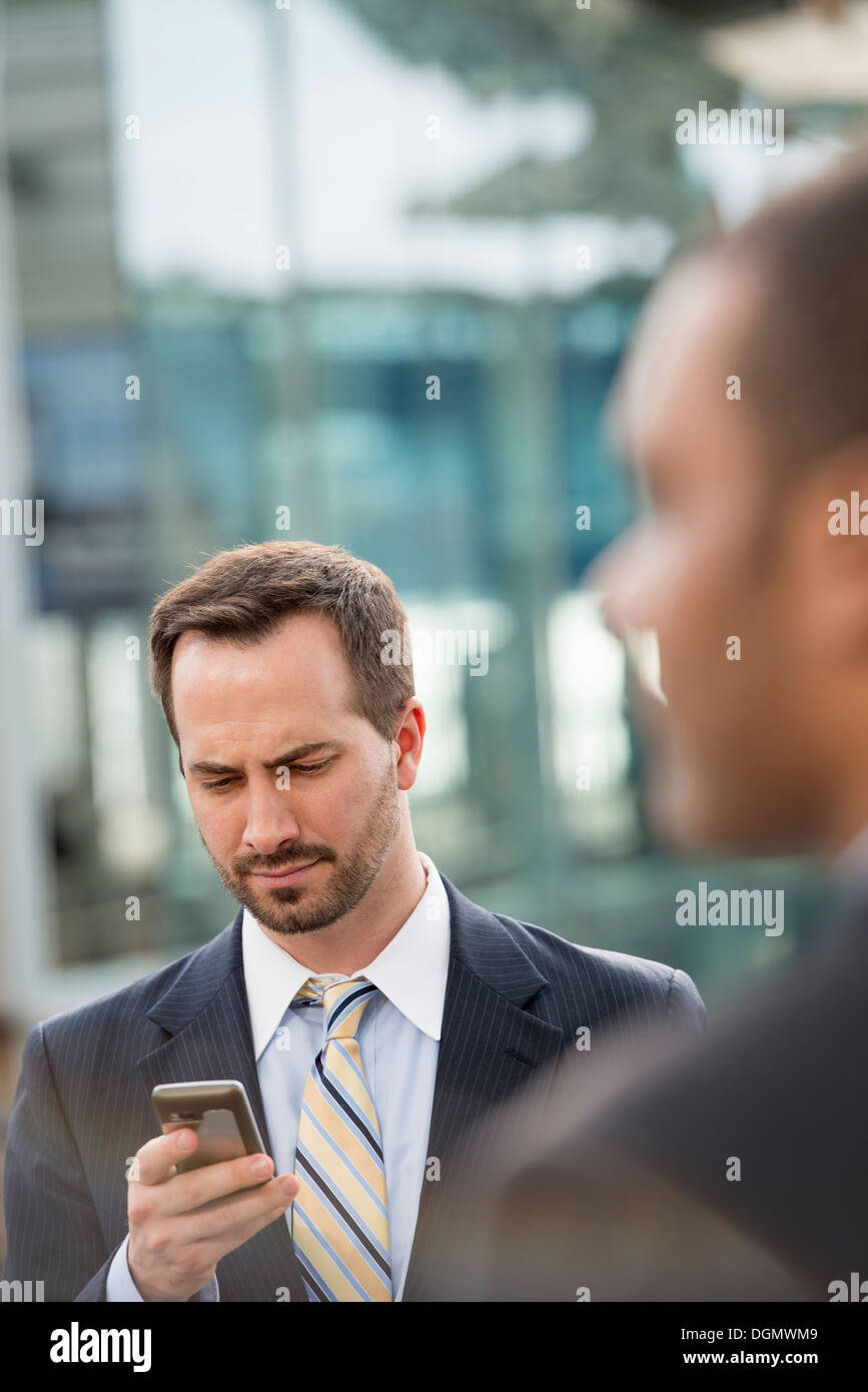 Città. Un uomo in un business suit controllare i suoi messaggi sul suo smart phone. Foto Stock