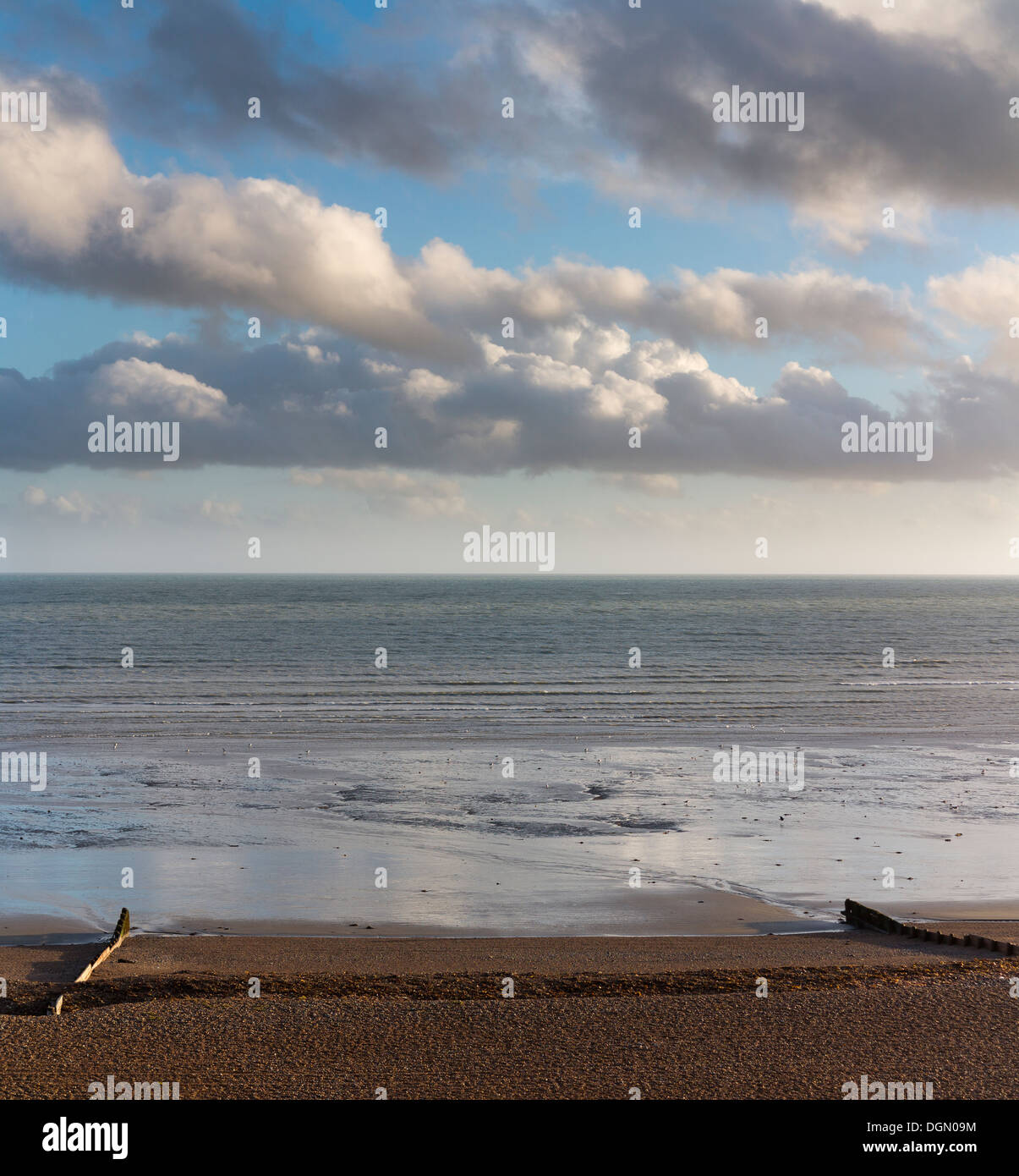 Guardando fuori su un mare calmo con il tardo pomeriggio di luce che riflette le nuvole in acqua calma tra due pennelli Worthing Inghilterra Foto Stock