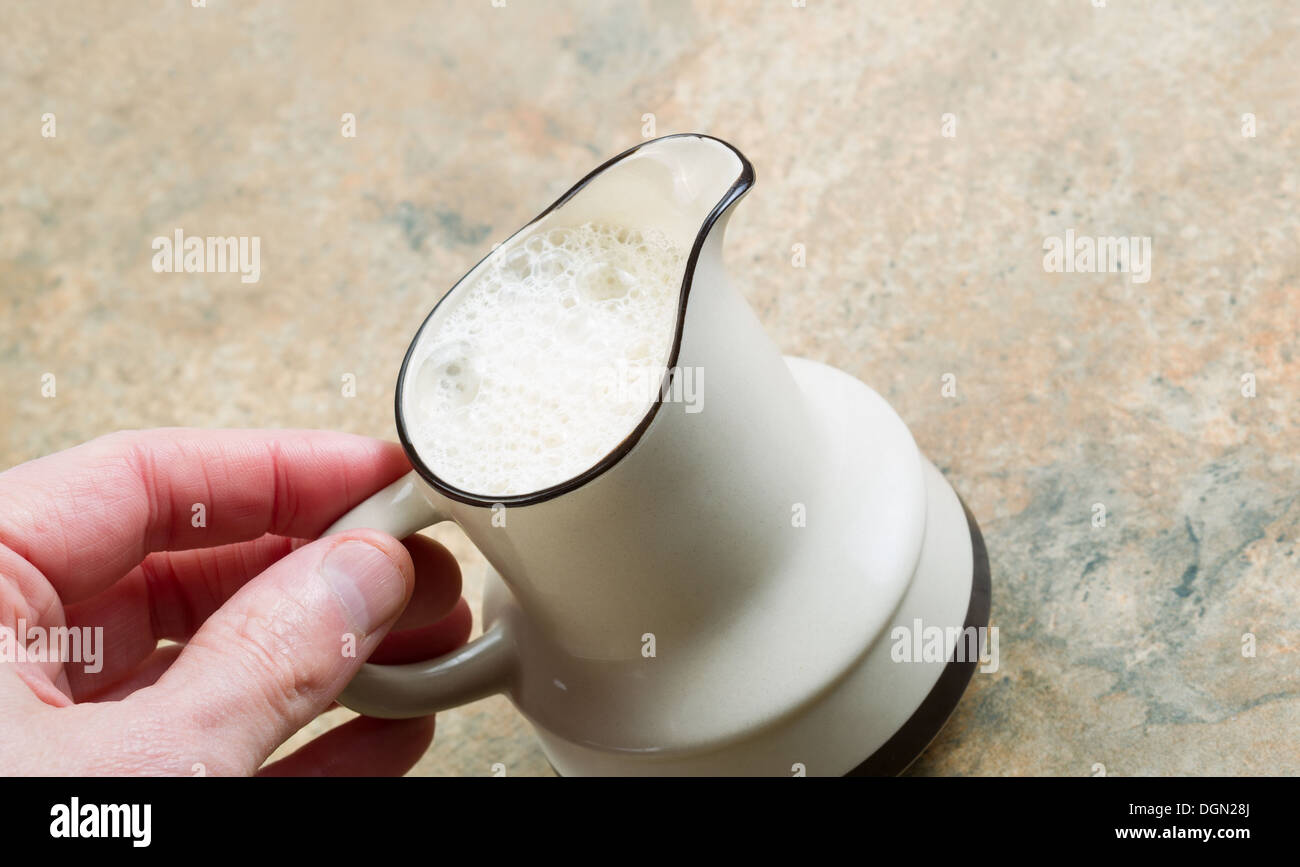 La foto in orizzontale dei maschi di mano azienda brocca del latte di mandorla con pietra bancone in background Foto Stock