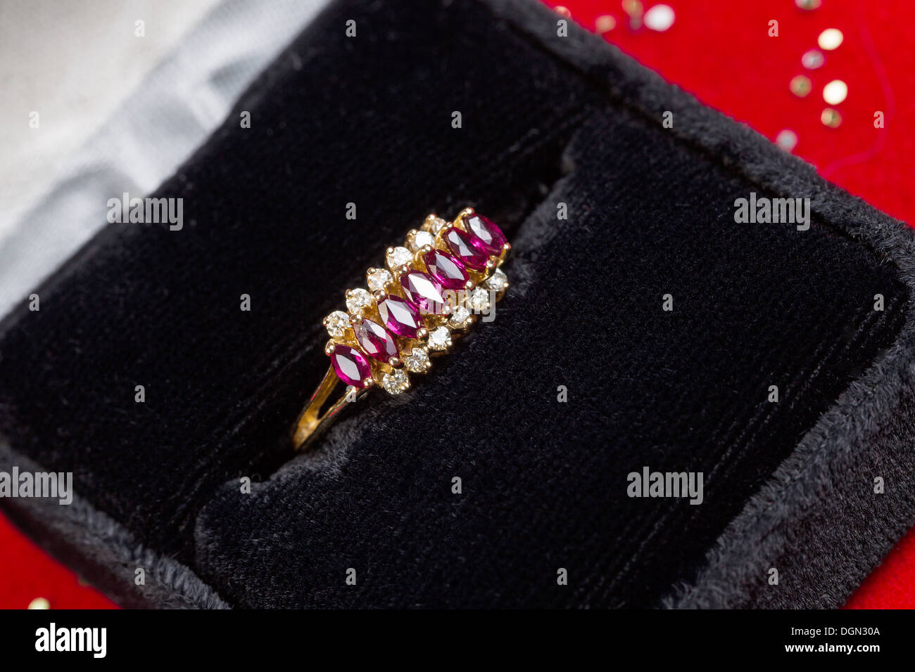 Foto orizzontale di Anello oro contenente pietre preziose e diamanti seduta all'interno della casella di gioielli su sfondo rosso Foto Stock