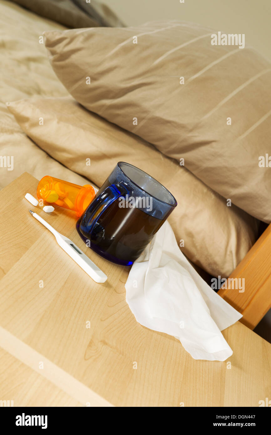 Foto verticale del bicchiere di tè caldo, termometro, tessuti e medicina sul cavalletto di notte con letto in background Foto Stock