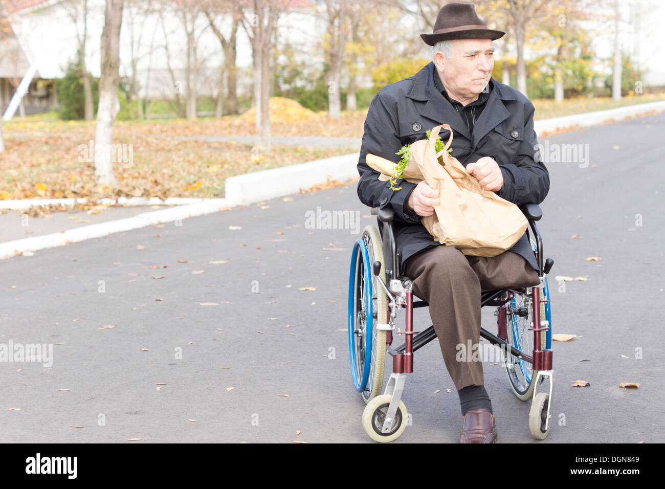 Uomo anziano in una sedia a rotelle a portare a casa la spesa al supermercato in un sacchetto di carta come egli siede in attesa in strada Foto Stock