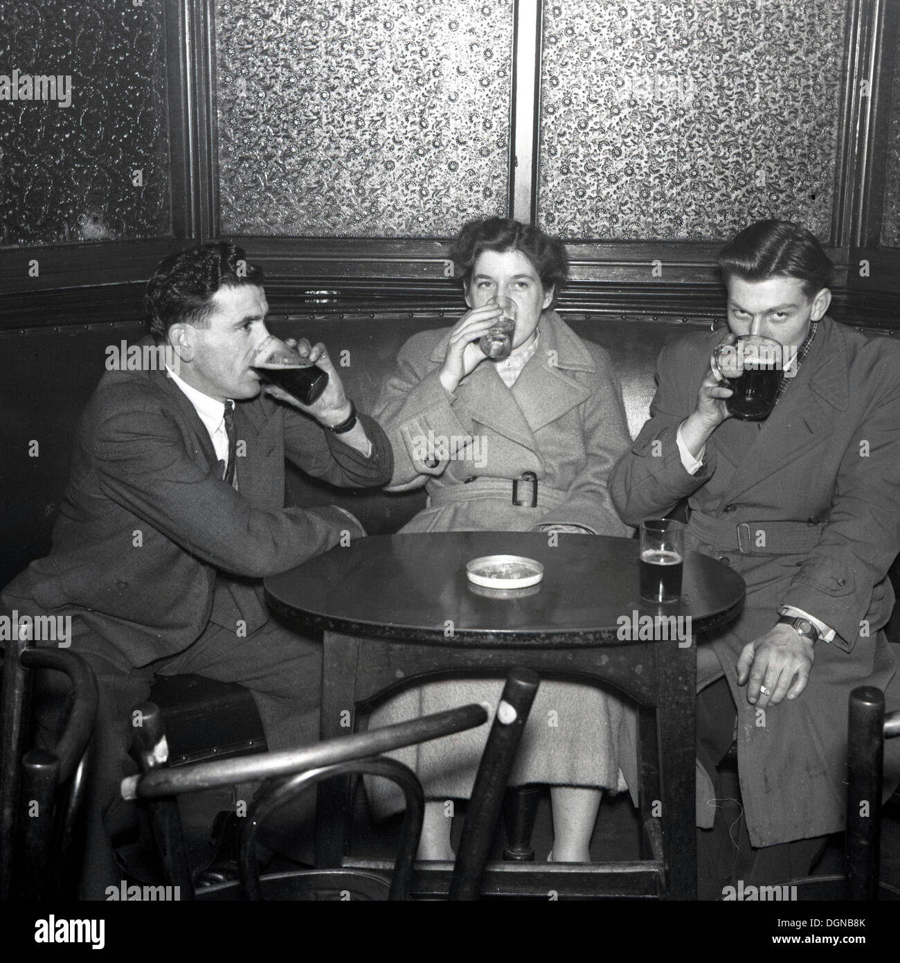 Foto storiche da anni cinquanta di due uomini adulti e una donna seduta e di bere insieme a una tavola rotonda in un bar o un accoppiamento preciso. Foto Stock