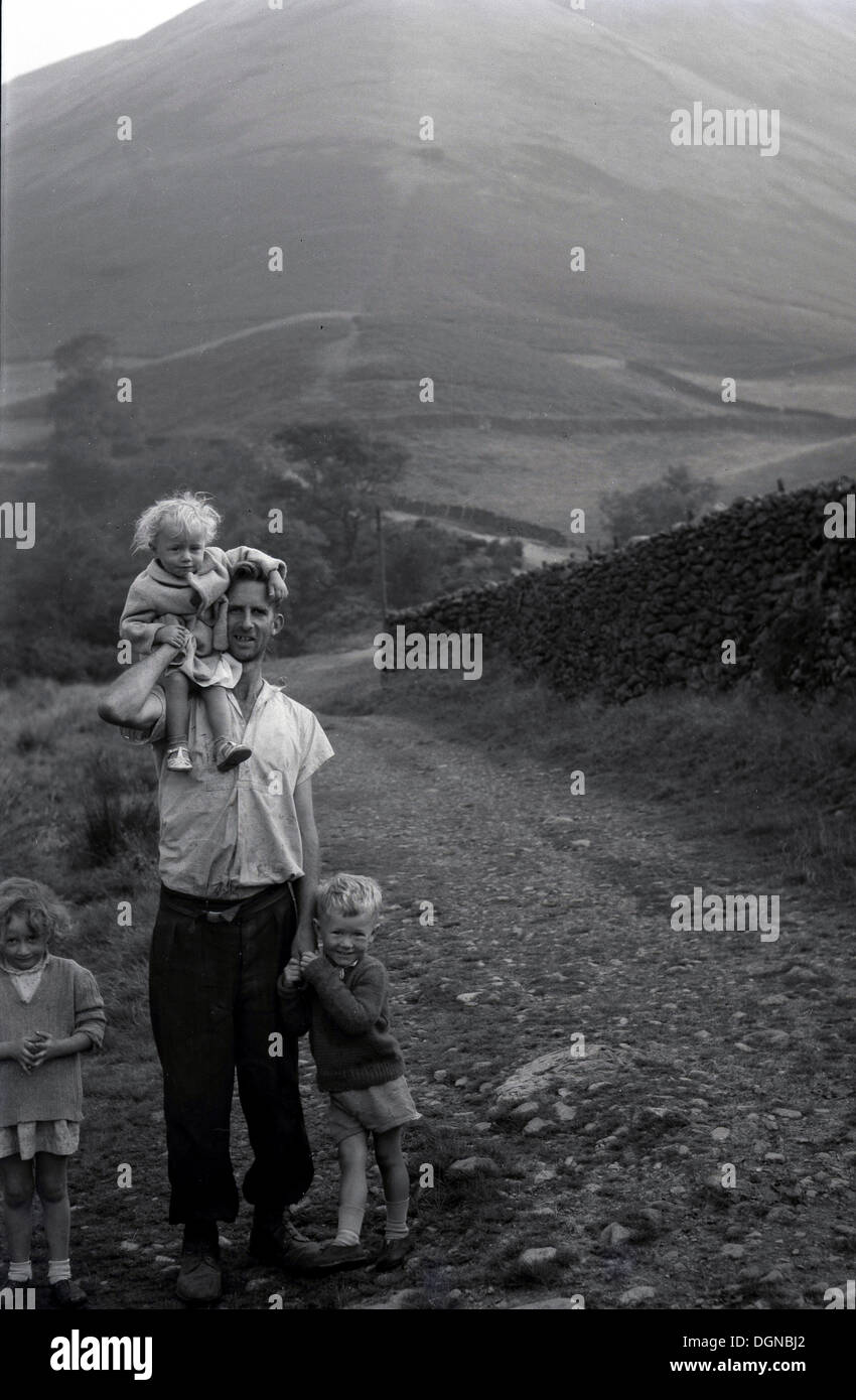 Anni '60, immagine storica, un padre si trova su una pista di ghiaia campagna in collina con i suoi tre bambini, uno che tiene la mano e uno la spalla, Somerset, Inghilterra. Foto Stock