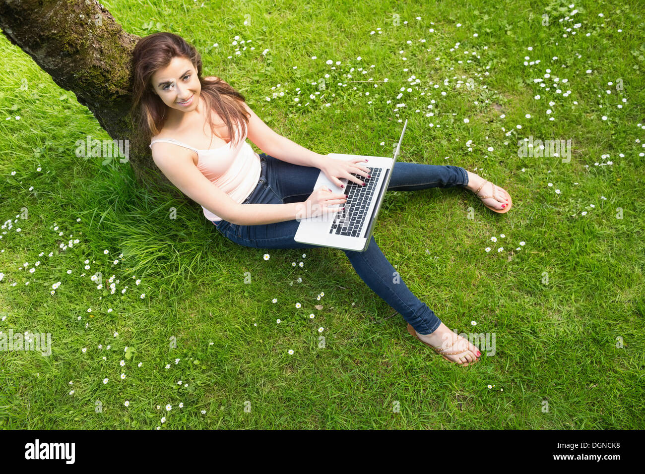 Bella donna appoggiata contro un albero utilizzando il notebook Foto Stock