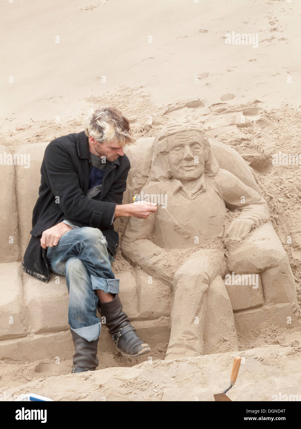 Scultore concentrandosi sulla creazione la scultura di sabbia di un uomo disteso su un divano, sul Fiume Tamigi South Bank di Londra, UK per suggerimenti Foto Stock