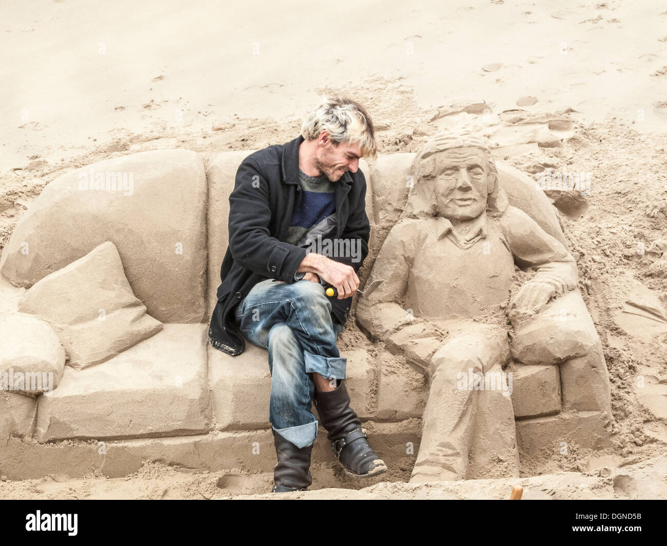 Scultore creando la scultura di sabbia di un uomo disteso su un divano, sul Fiume Tamigi South Bank di Londra, UK per suggerimenti Foto Stock