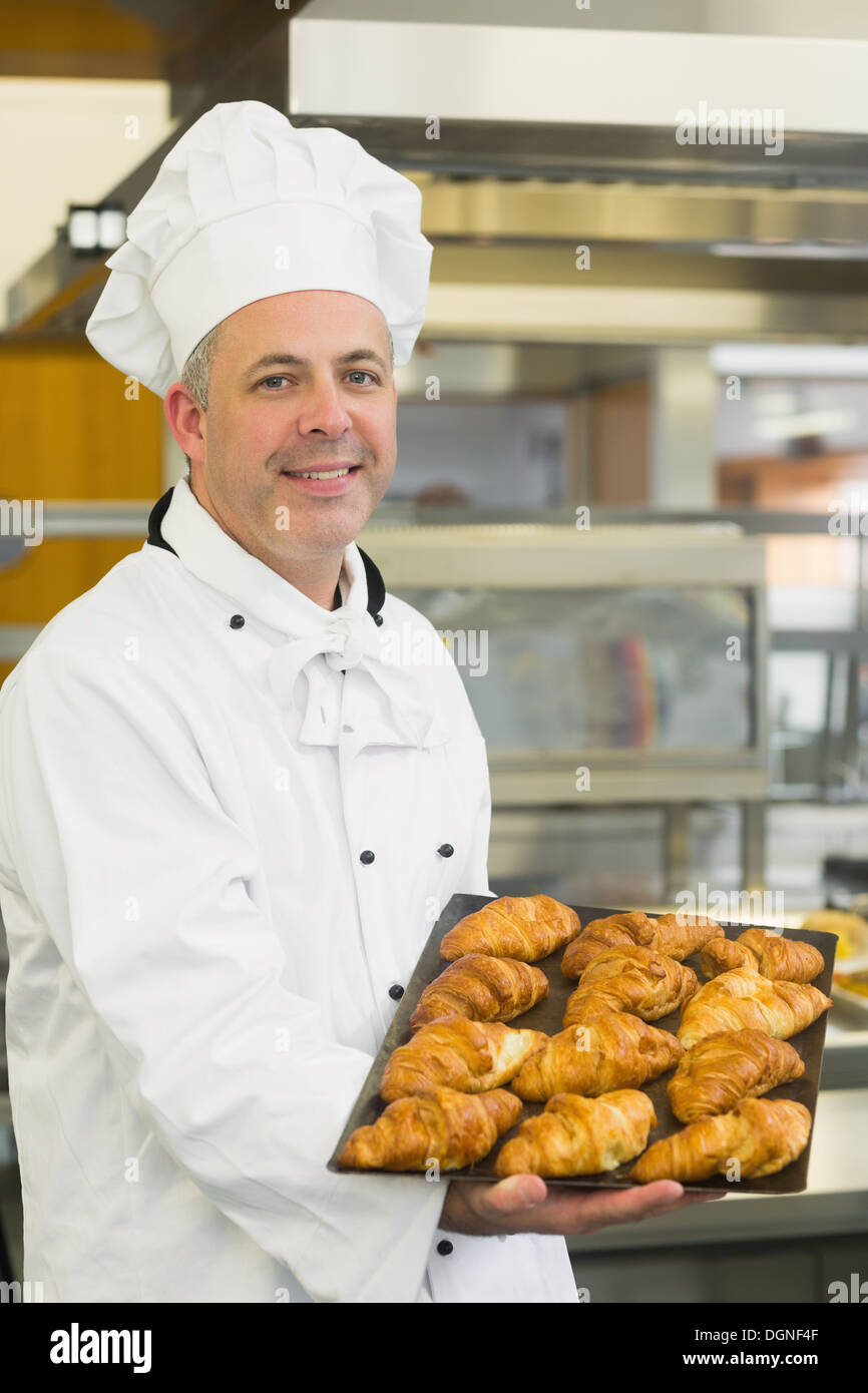 Baker che mostra alcuni croissant su un vassoio da forno Foto Stock