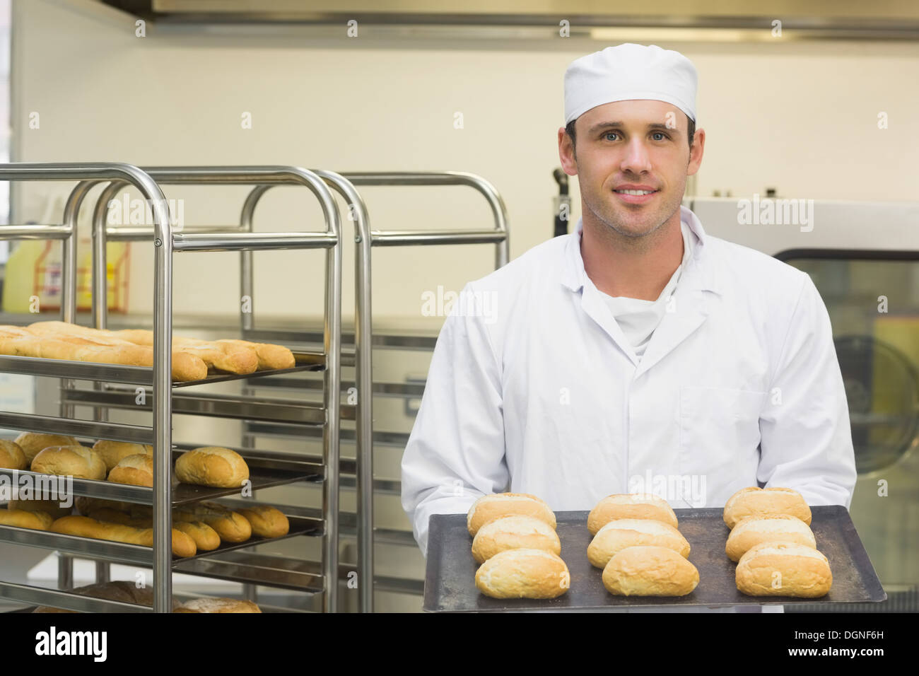 Felice giovani baker holding alcuni rotoli su un vassoio da forno Foto Stock