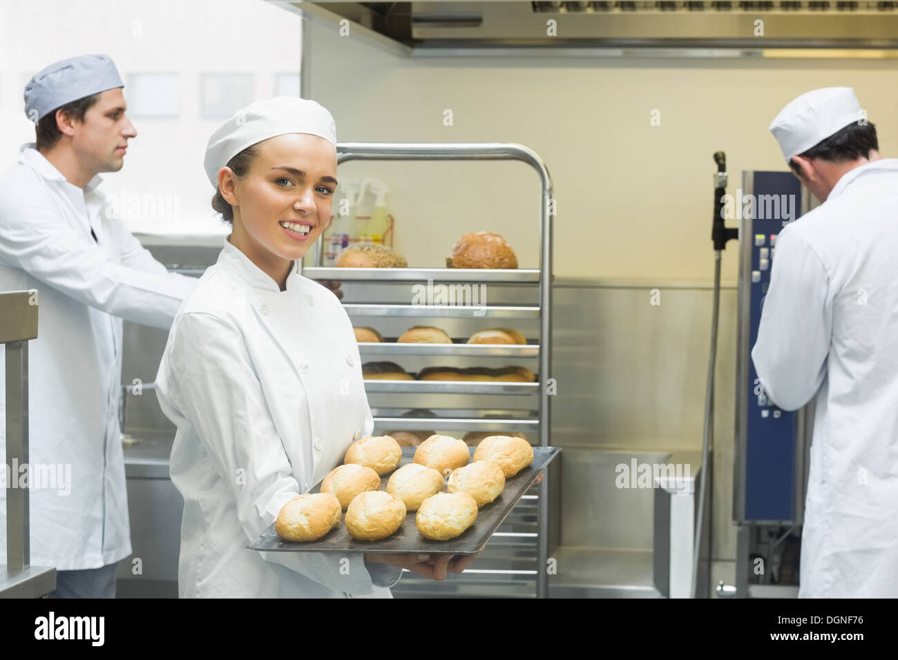 Carino giovane femmina baker tenendo un vassoio da forno con i rotoli su di esso Foto Stock