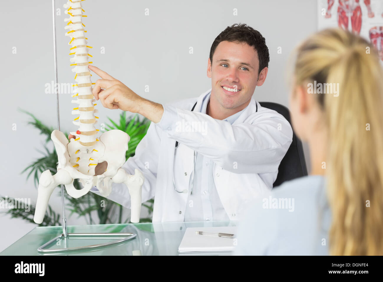 Medico sorridente che mostra un paziente qualcosa sul modello dello scheletro Foto Stock