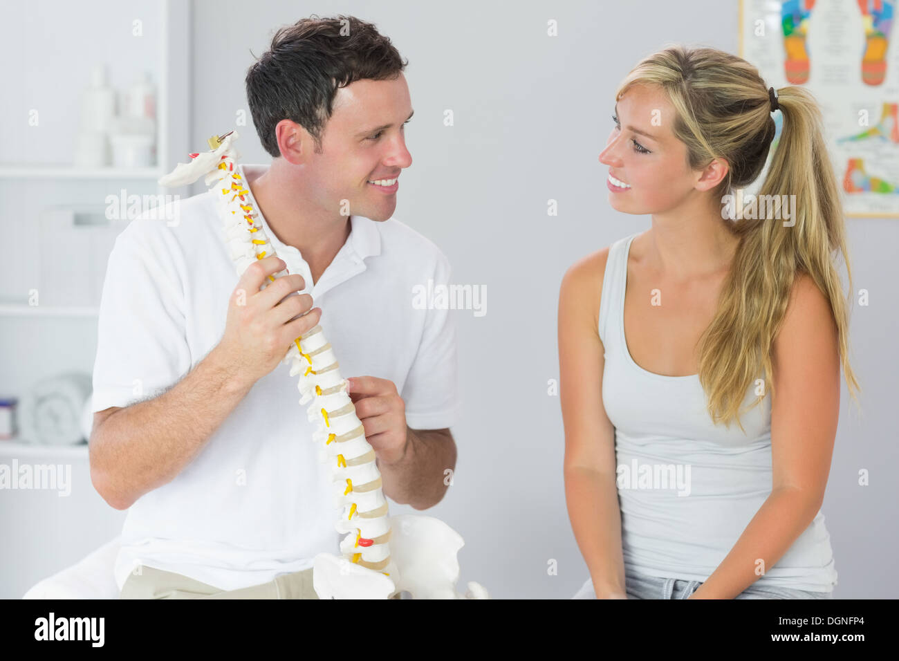 Sorridente fisioterapista paziente mostrando qualcosa sul modello dello scheletro Foto Stock