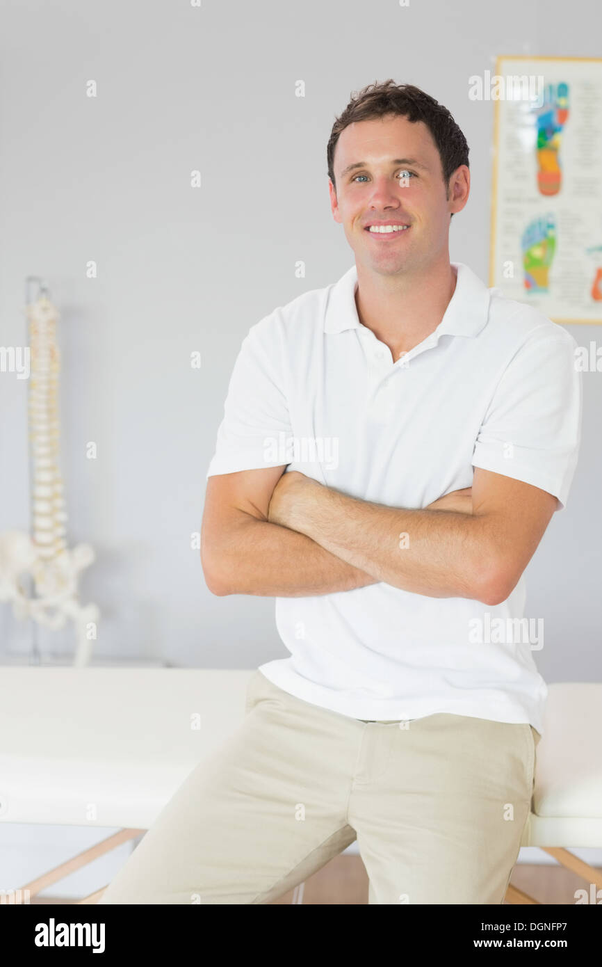 Bello felice fisioterapista seduto con le braccia incrociate Foto Stock