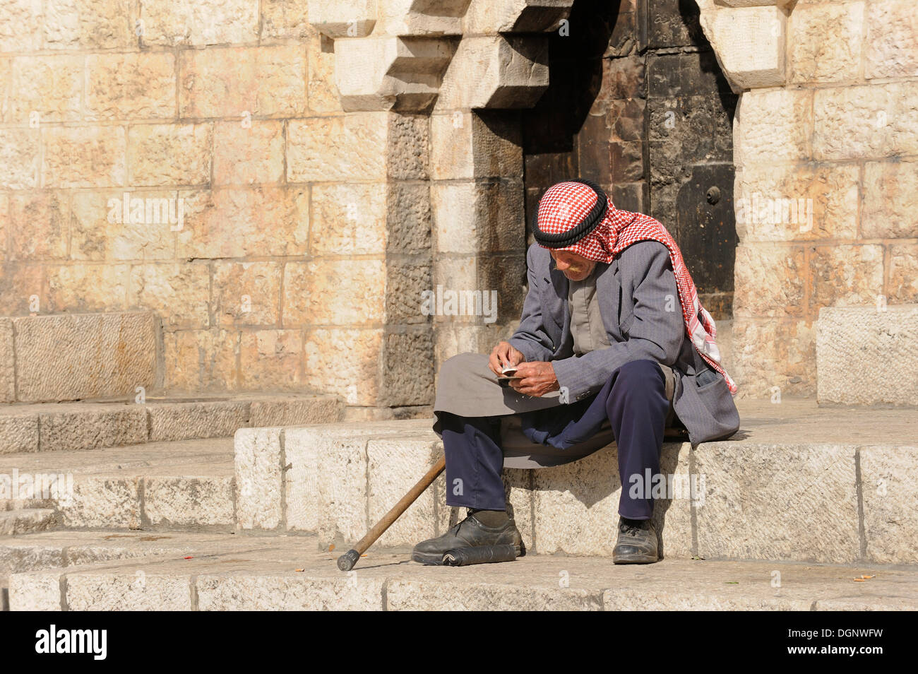 Uomo palestinese con keffiyeh o kafiya seduta sul suo proprio sui gradini della porta di Damasco, città vecchia, Gerusalemme, Israele Foto Stock