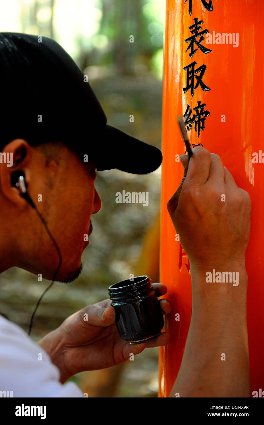L'uomo scrivendo il nome di donatori con un pennello su di un torii, Fushimi Inari Taisha Sacrario scintoista, Fushimi, Kyoto Kinki regione Foto Stock