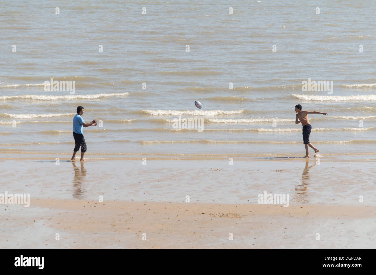 Lanciare una palla da rugby sulla spiaggia Foto Stock