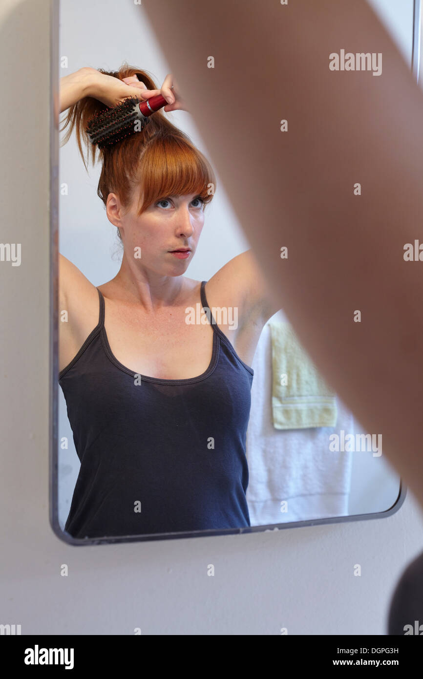 Metà donna adulta spazzolare i capelli in specchio Foto Stock