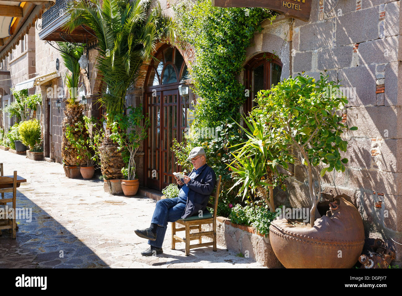 Uomo seduto su una sedia davanti a un hotel, Assos, Çanakkale provincia, regione di Marmara, Turchia Foto Stock