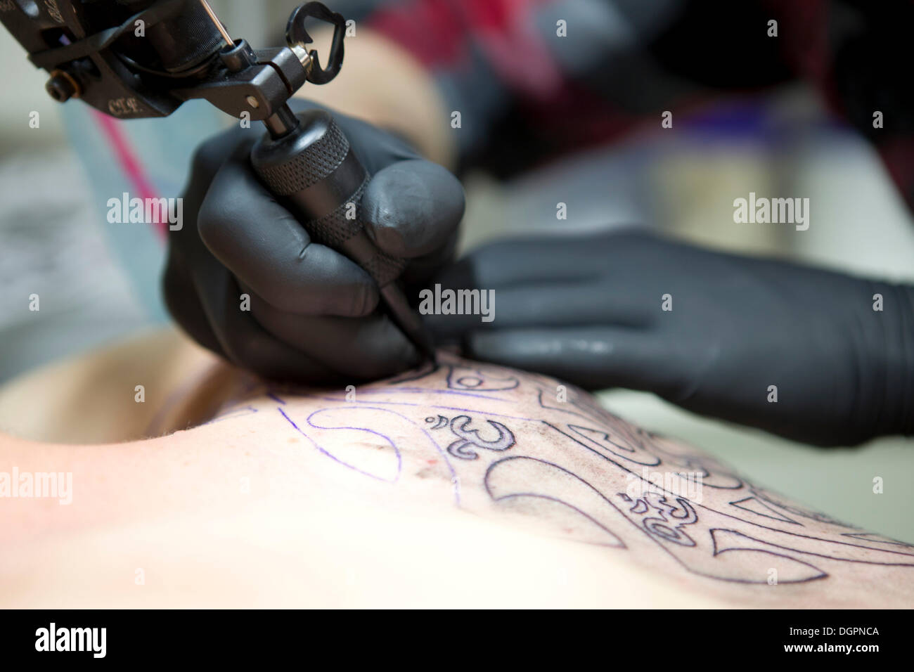 Le mani di un tatuaggio artista con un dermografo applicando un tatuaggio su una spalla Foto Stock