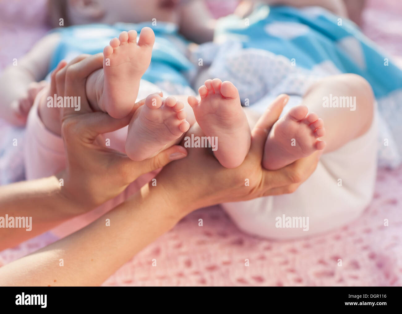 Gambe neonati in mano ai genitori. Gemelli giacente su una coperta rosa. Foto Stock