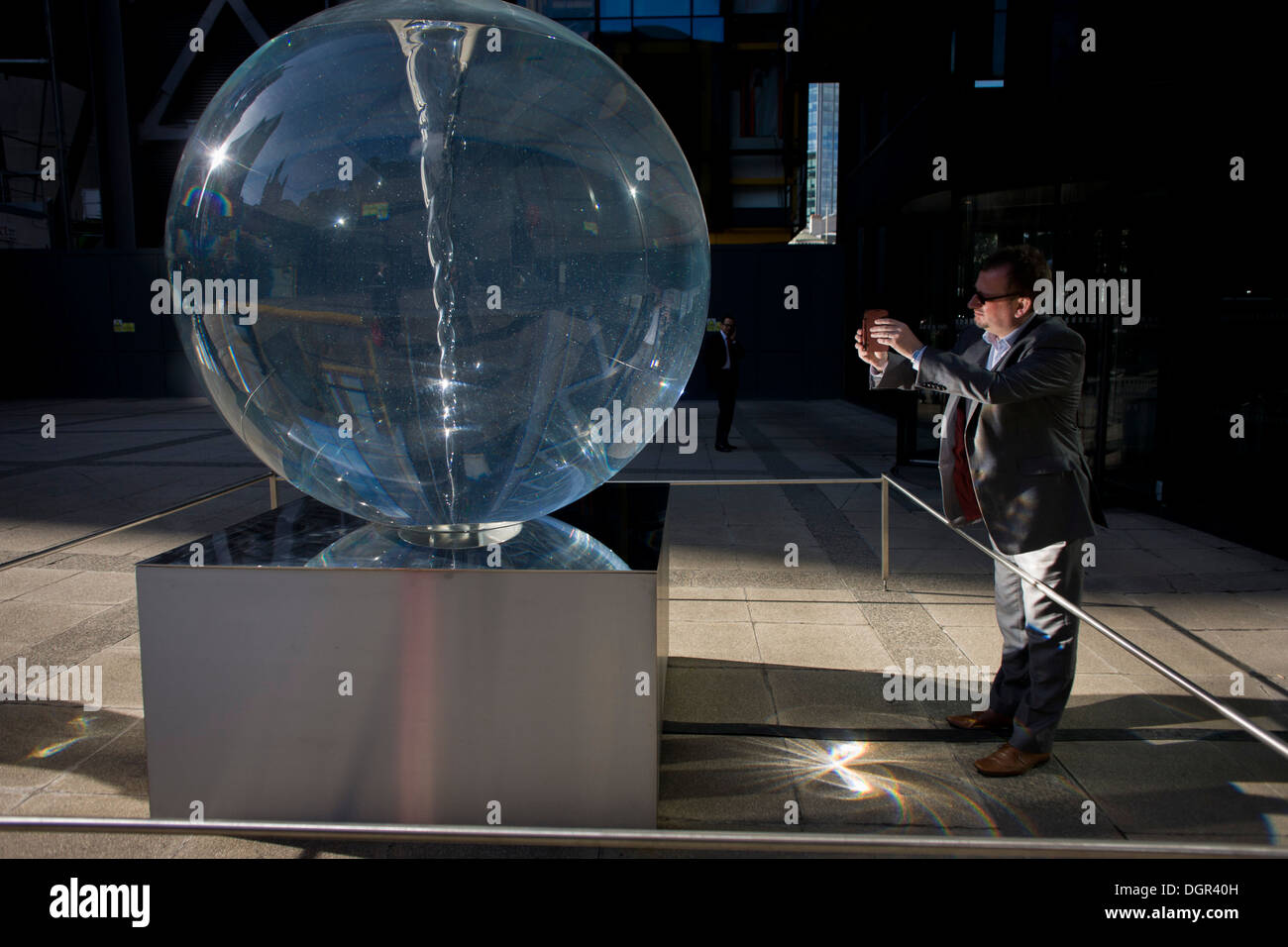 Distorsione visto attraverso Petroc Sesti di instillazione di arte chiamato tempo piega nella grande Helen Square nella città di Londra. Con una forte luce solare rifratta sul terreno, la luce rimbalza nella faccia di passaggio di un imprenditore come egli prende le foto con uno smartphone. Petroc Sesti è una base a Londra artista britannico e ora si piega piega la luce come un prisma, hypnotising visualizzatore riflettendo sulla sua mutevole moto a spirale. Foto Stock