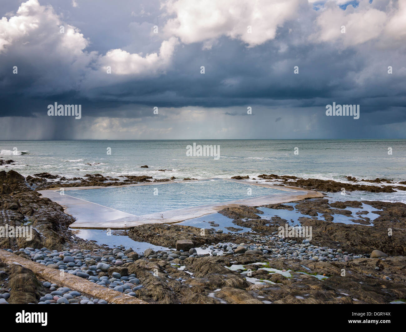 La piscina Rock Pool del Westward ho! E una tempesta estiva sull'Atlantico in lontananza sulla costa nord del Devon, Inghilterra. Foto Stock