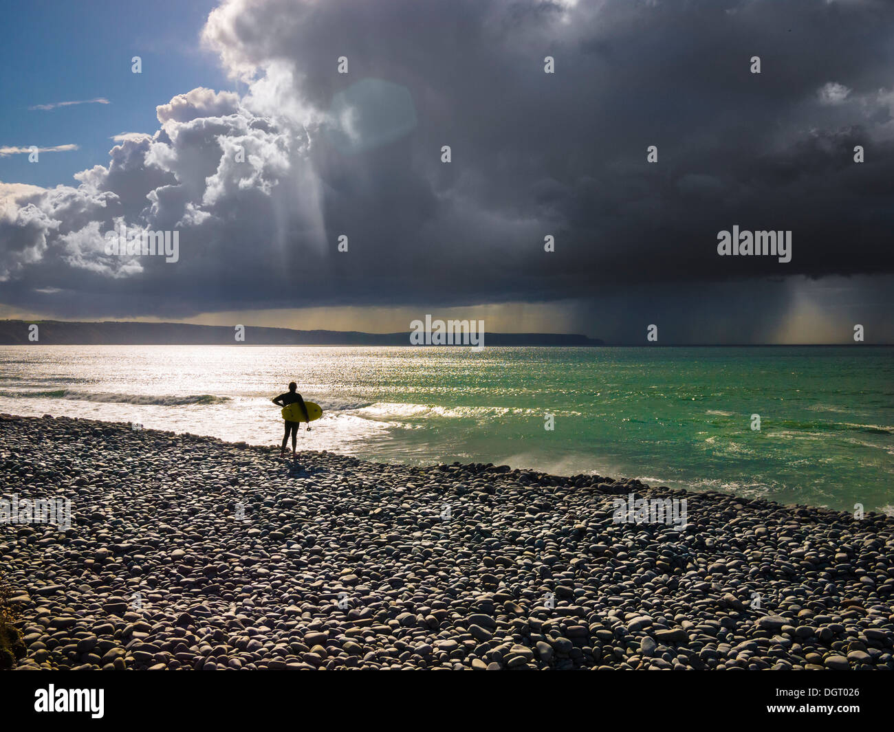 Surfer si trovava su una spiaggia di ciottoli che si affaccia sul mare con una tempesta in lontananza. Cornborough Range, Abbotsham, North Devon, Inghilterra. Foto Stock