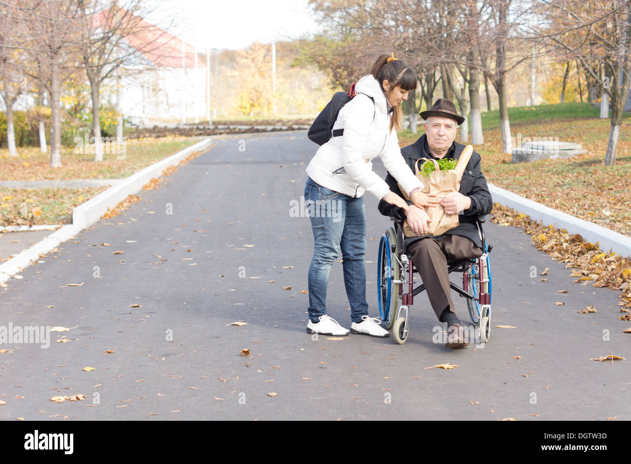 Figlia di consegnare un anziano uomo disabili in sedia a rotelle un sacco di generi alimentari come si prepara a spingerlo lungo la strada dopo che lo shopping. Foto Stock
