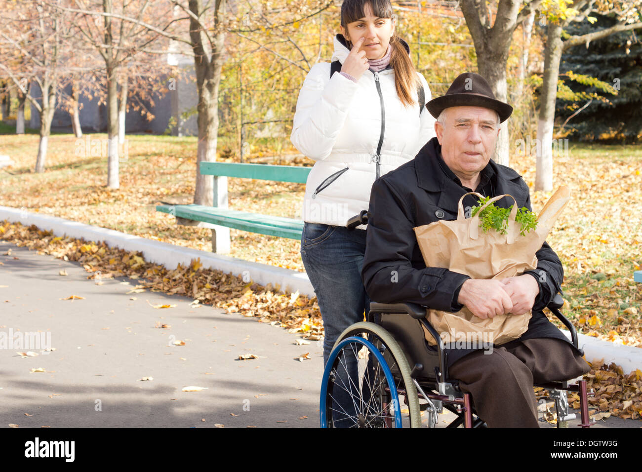 Donna aiutare un anziano uomo disabili in sedia a rotelle prendendo lui fuori a fare la spesa come essi ritornano insieme lungo la strada con la sua spingendo la sedia a rotelle. Foto Stock