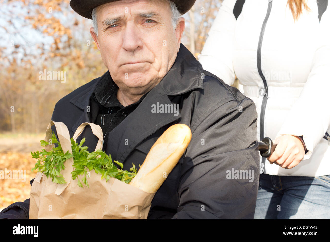 Senior uomo con i suoi negozi di generi alimentari in una sedia a rotelle come egli viene spinto lungo la strada da una femmina caregiver dopo andare a fare la spesa per i prodotti alimentari Foto Stock