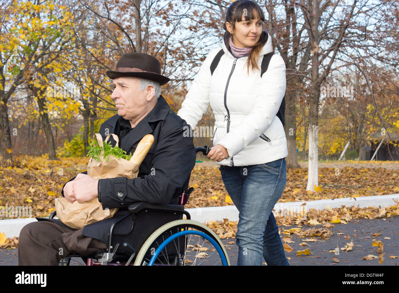 Donna felice aiutare un anziano uomo disabile che lo spinge lungo la strada nella sua sedia a rotelle dopo aver preso lui fuori a fare la spesa. Foto Stock