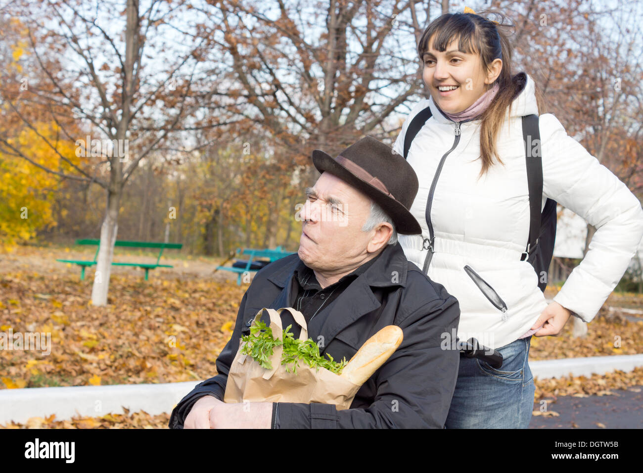 Donna felice con il suo anziano padre disabili sostando in strada per raddrizzare la sua camicia come lei lo spinge lungo nella sua sedia a rotelle mentre sono fuori a fare la spesa. Foto Stock