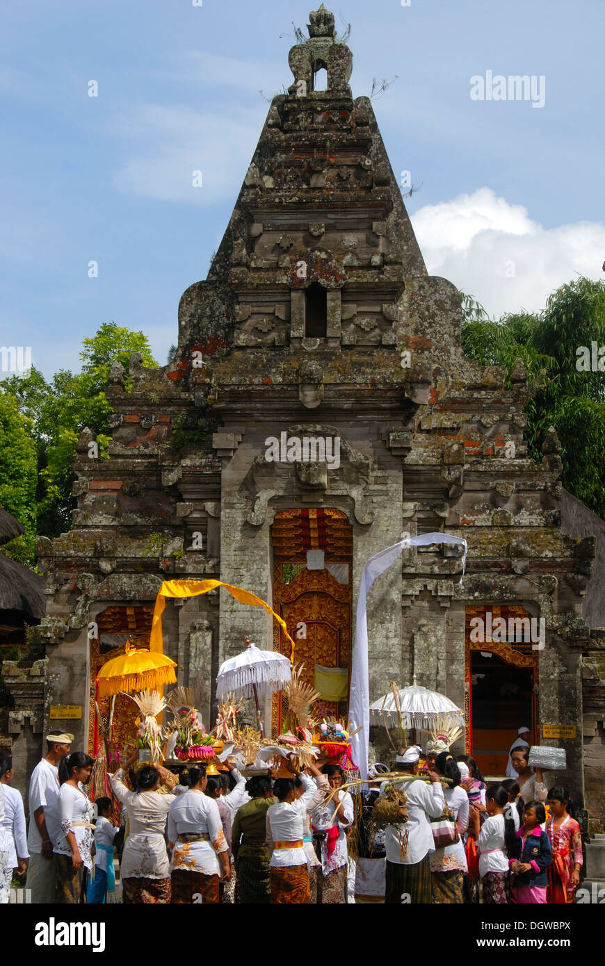 L Induismo di Bali, credenti, donne vestiti a festa le offerte di trasporto e ombrelloni, torre del tempio Foto Stock