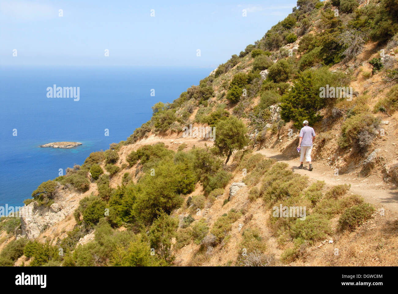 Donna trekking lungo una ripida scogliera costiera trail, guardando sopra un'isola e il blu del mare, discendente da Moutti tis Sotiras Foto Stock