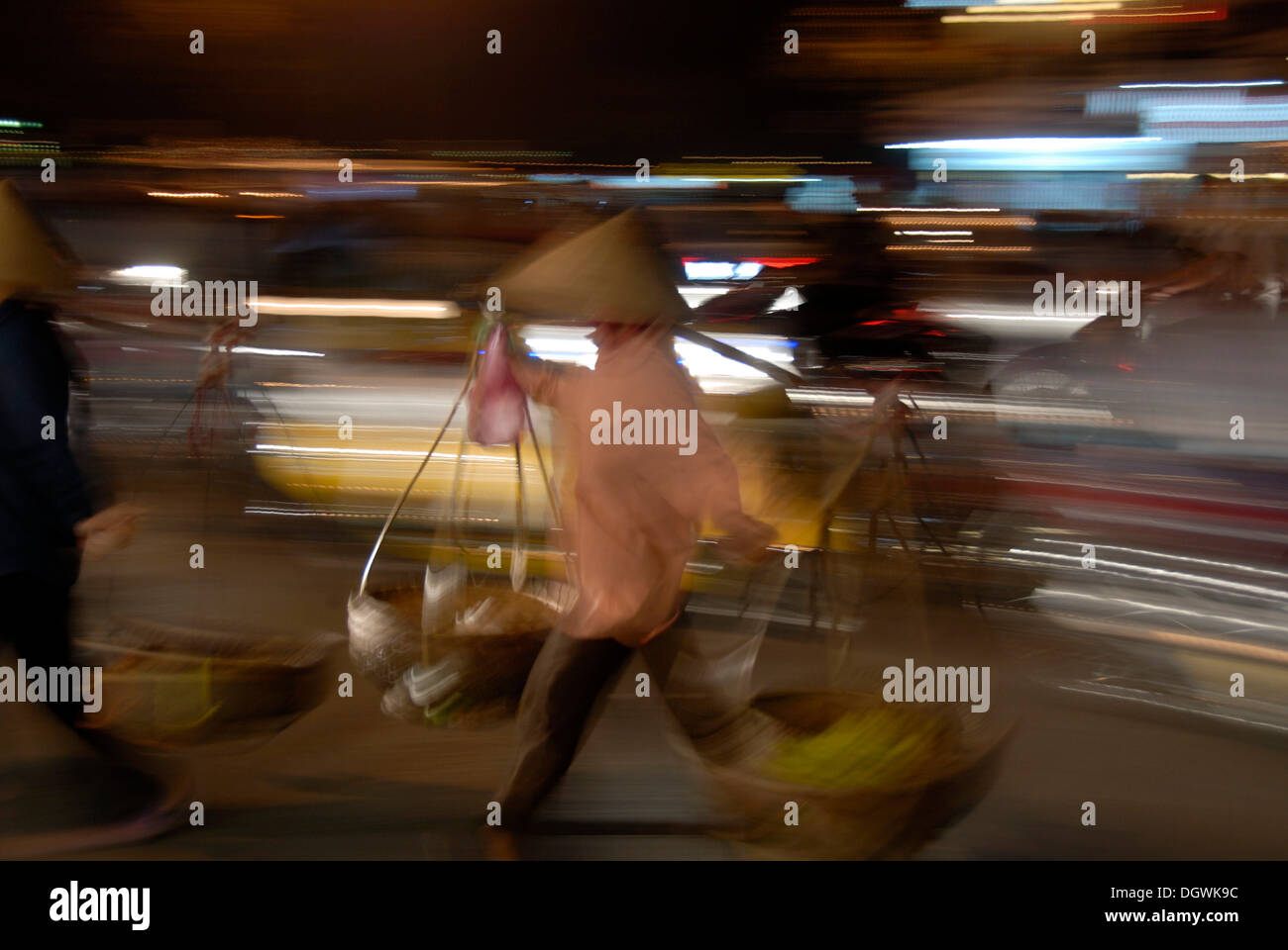 Donna vietnamita cestelli porta sulle sue spalle attraverso il traffico di notte, motion blur, Hanoi, Vietnam Asia Foto Stock