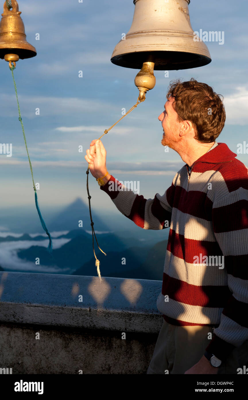 L uomo lo squillo di una campana in un tempio buddista, Adam's Peak, Sri Pada, Dalhousie, Zentrales Hochland, Sri Lanka Foto Stock