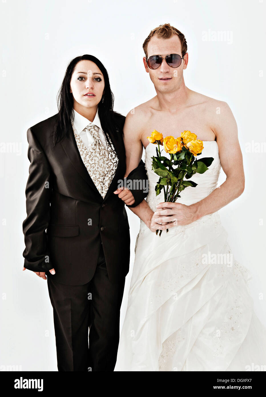 Sposa indossa una tuta e una per lo sposo che indossa un abito da sposa con occhiali da sole e rose giallo Foto Stock
