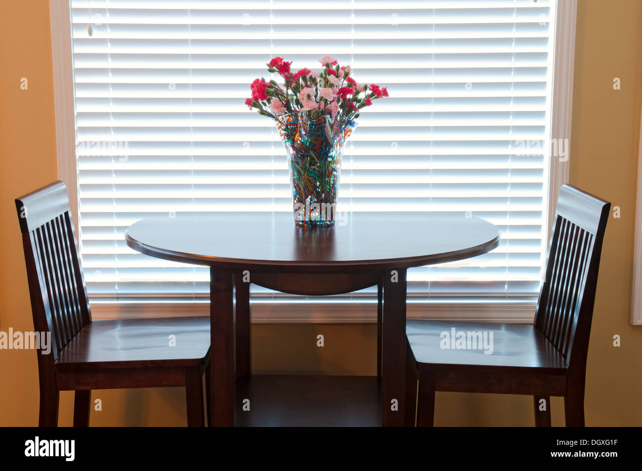 Tavolo da pranzo e sedie decorate con fiori in interni con retroilluminazione Foto Stock
