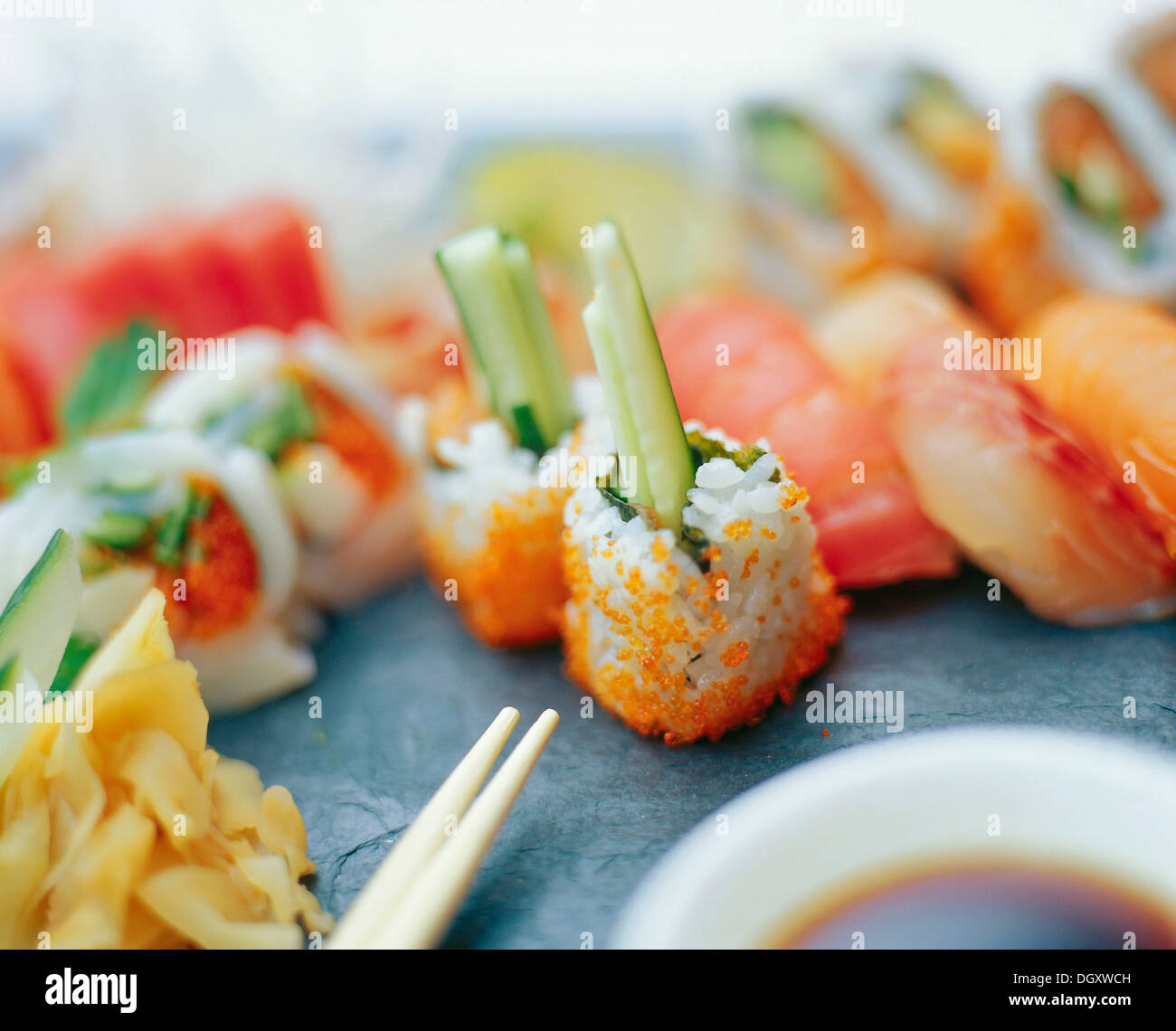 Un assortimento di sushi rotoli con zenzero sott'aceto e bastoncini su una superficie di ardesia Foto Stock