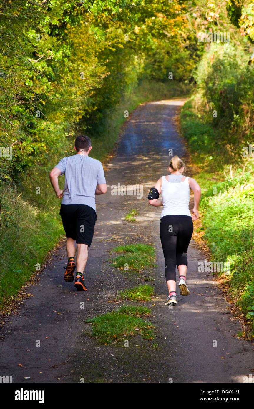 Due pareggiatori per uomo e donna in corsa jogging giù un rurale Somerset lane Foto Stock