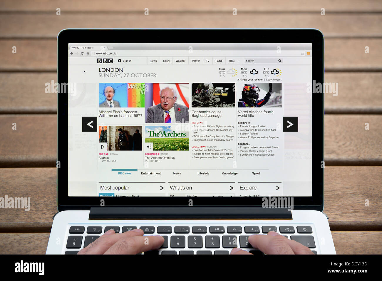 La BBC Online sito web su un computer MacBook contro una panca in legno sfondo all'aperto tra cui un uomo le dita (solo uso editoriale). Foto Stock