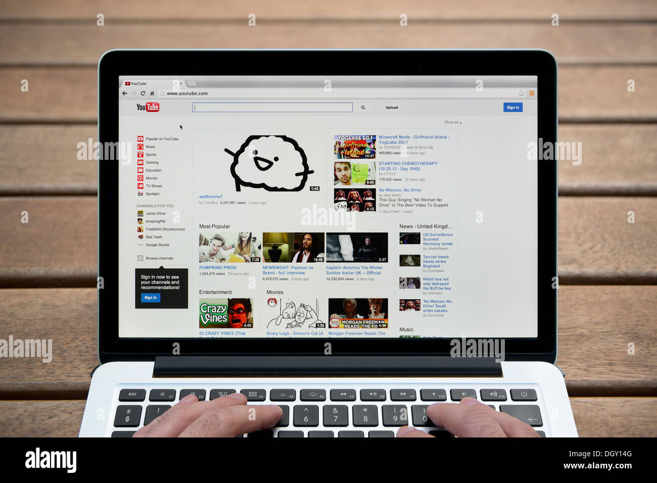 Il sito web di YouTube su un MacBook contro una panca in legno sfondo all'aperto tra cui un uomo le dita (solo uso editoriale). Foto Stock