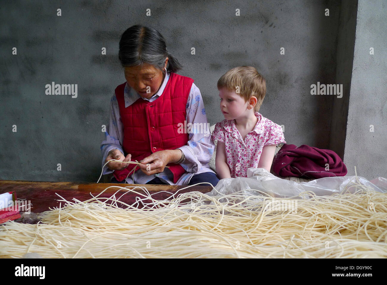 Incontra in Cina, giovane ragazza europea guarda su una vecchia donna cinese rendendo i bastoncini di incenso, Moxi, Hailuogou, Sichuan, in Cina Foto Stock