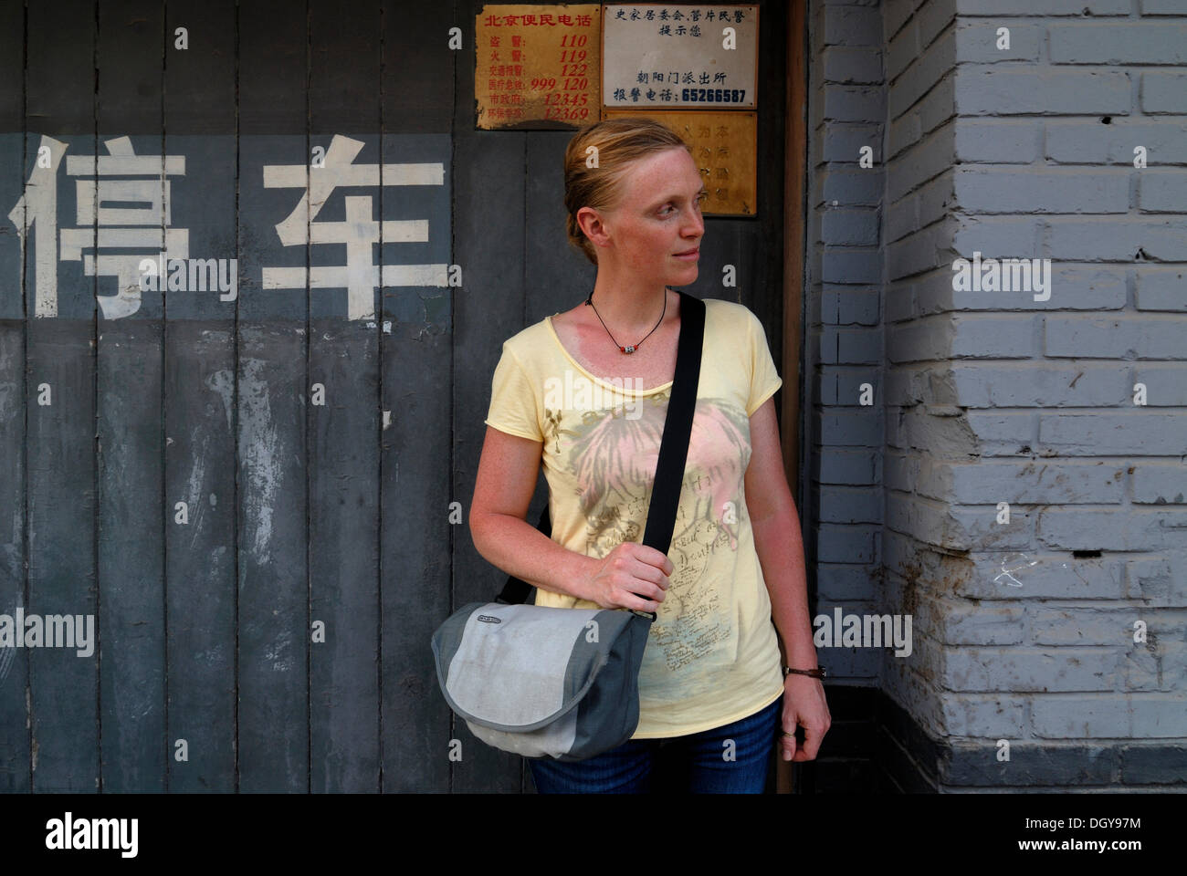 I capelli rossi della donna che porta una borsa a tracolla in piedi di fronte a una casa su un cinese Hutong, una strada stretta Foto Stock