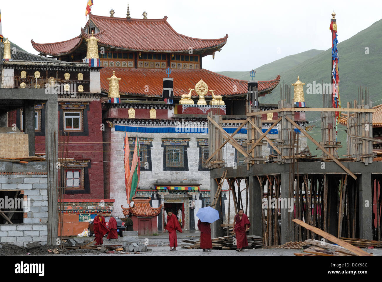 I monaci del Tibet in rosso di accappatoi e permanente a piedi sotto la pioggia attraverso il sito in costruzione presso il monastero Lhagang Foto Stock