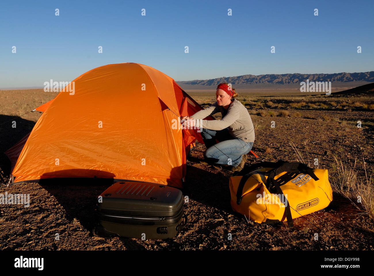 Giovane donna impostazione di camp con orange tenda da trekking e da attrezzature utilizzate all'aperto nel Deserto del Gobi, Khorgoryn Els Foto Stock