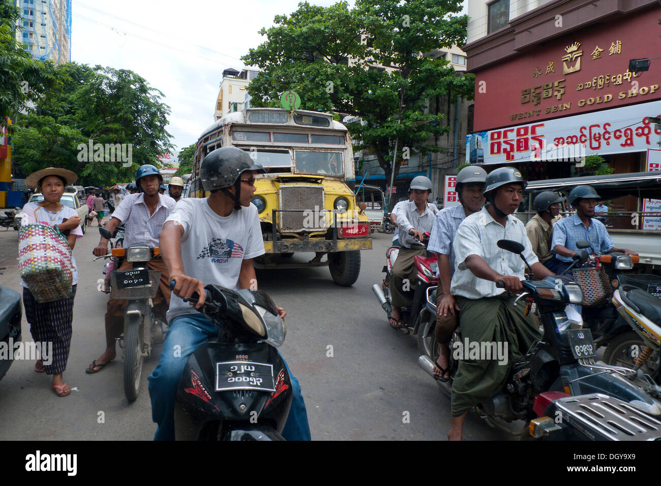 Scena di strada, birmani gli uomini a cavallo ciclomotori o scooter, pedoni, vecchio bus birmano sulla strada per il mercato a Mandalay, Birmania Foto Stock